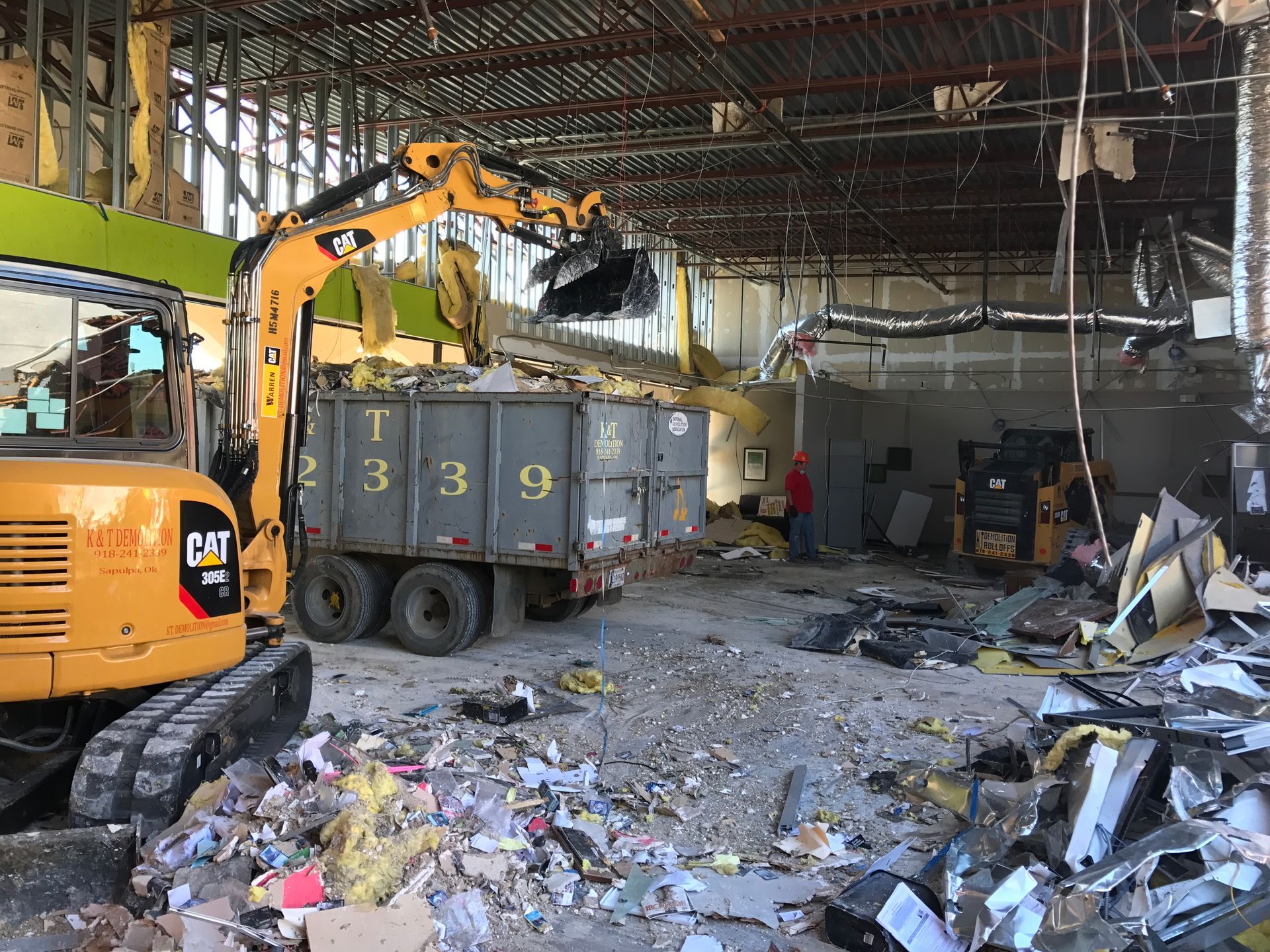 Yellow excavator loading debris into a dump truck inside a building demolition site.
