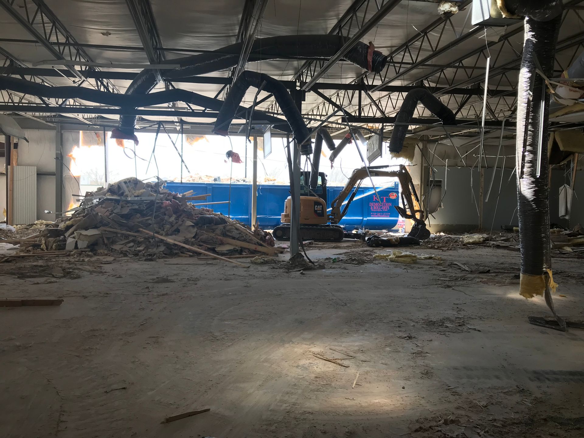 Demolished interior with debris pile and small excavator.