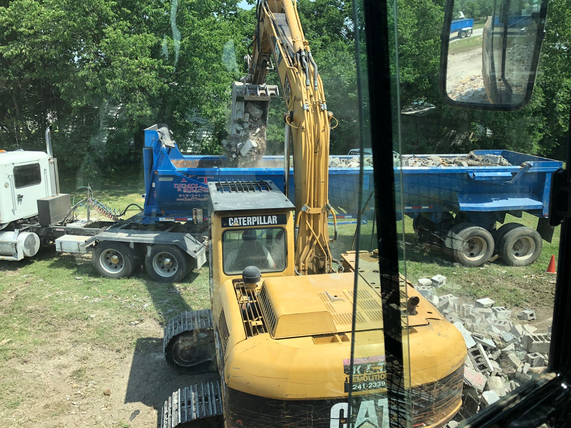 Yellow excavator loading debris into a blue dump truck.