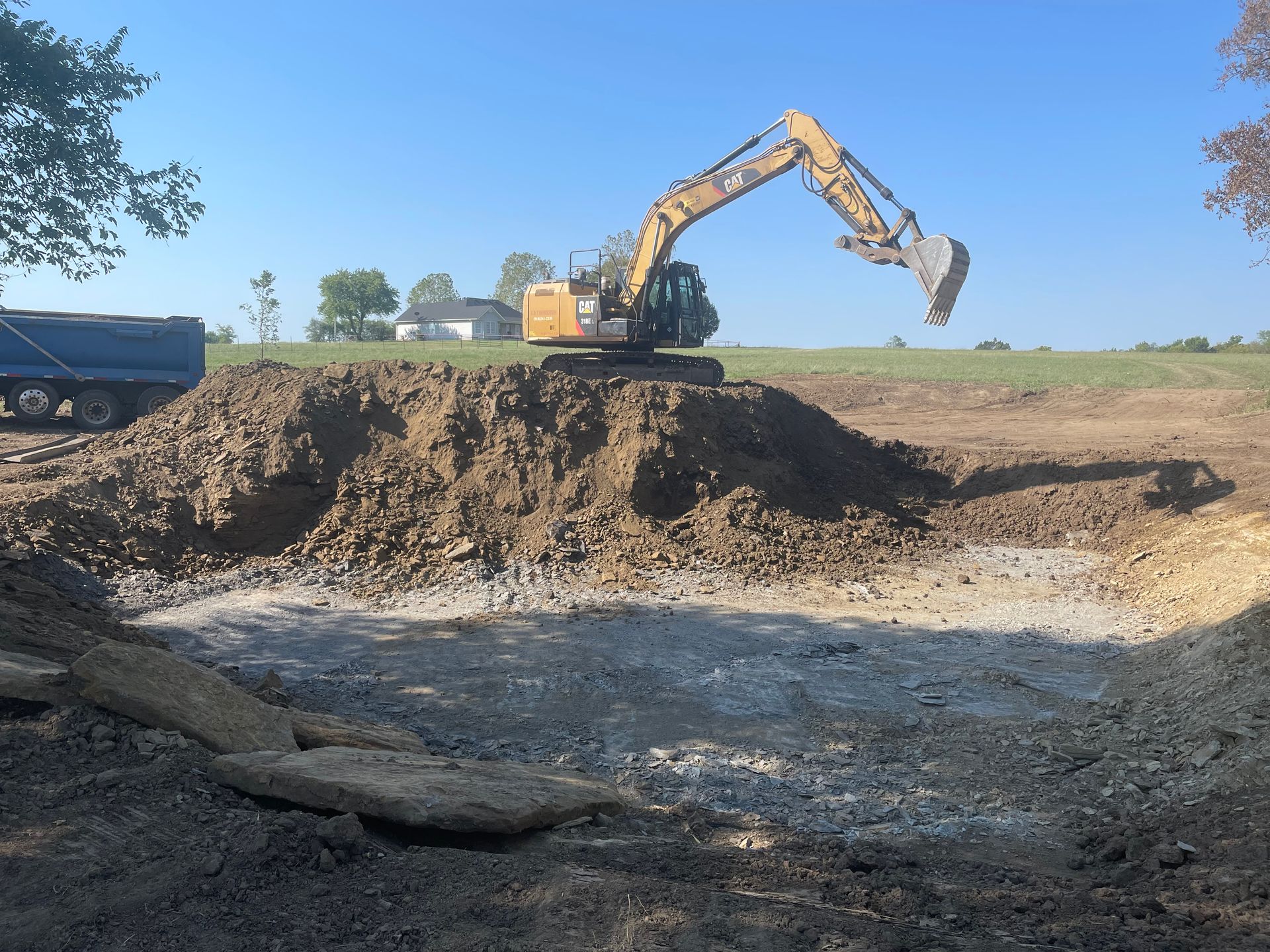 Excavator digging in dirt pile. Blue sky, flat field.