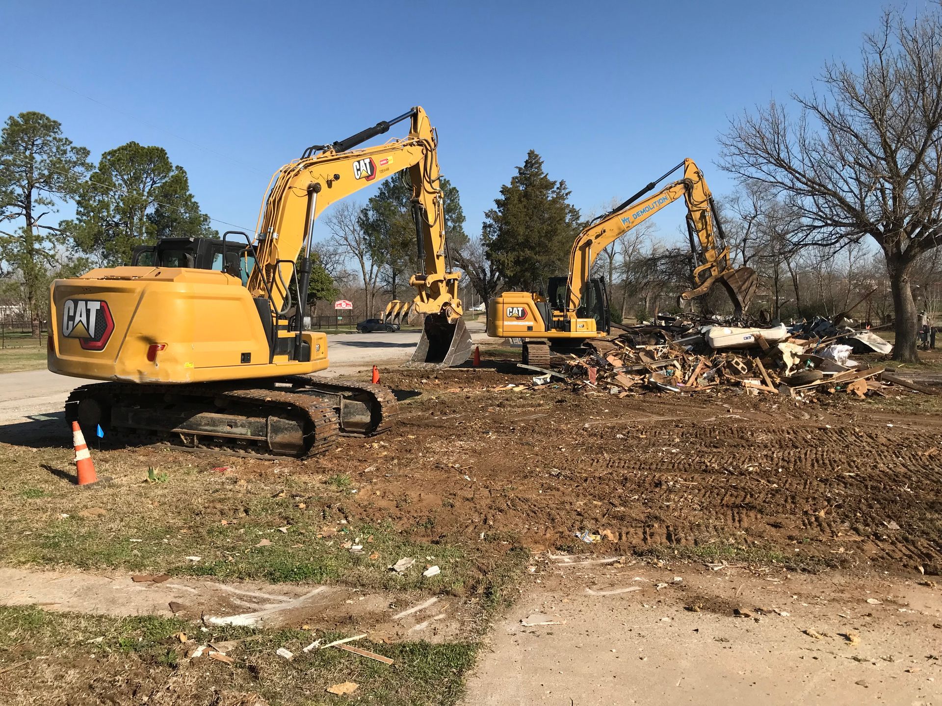 Two yellow Caterpillar excavators demolishing a building on a sunny day.