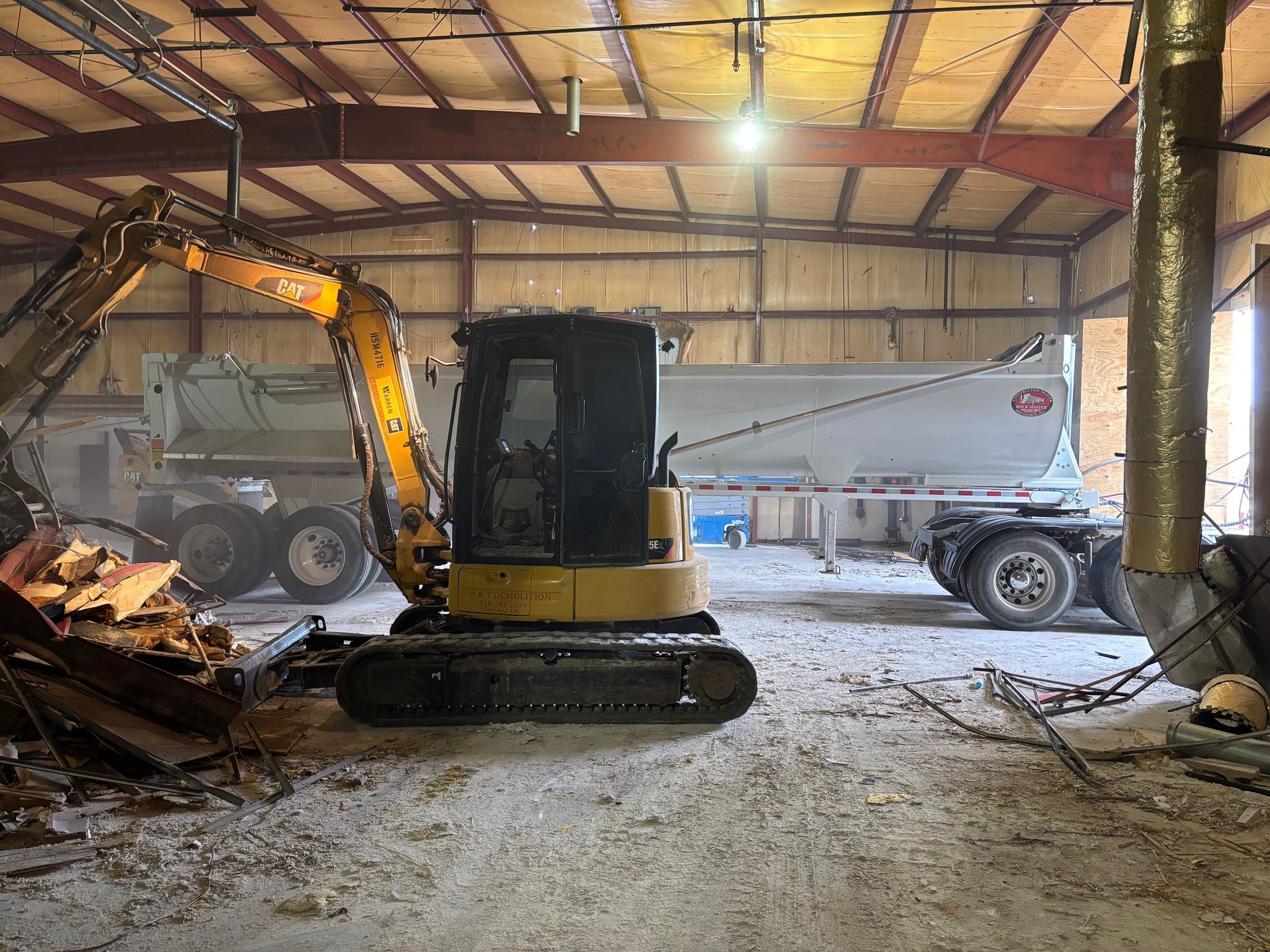 Excavator inside a building next to a dump truck, demolition in progress.