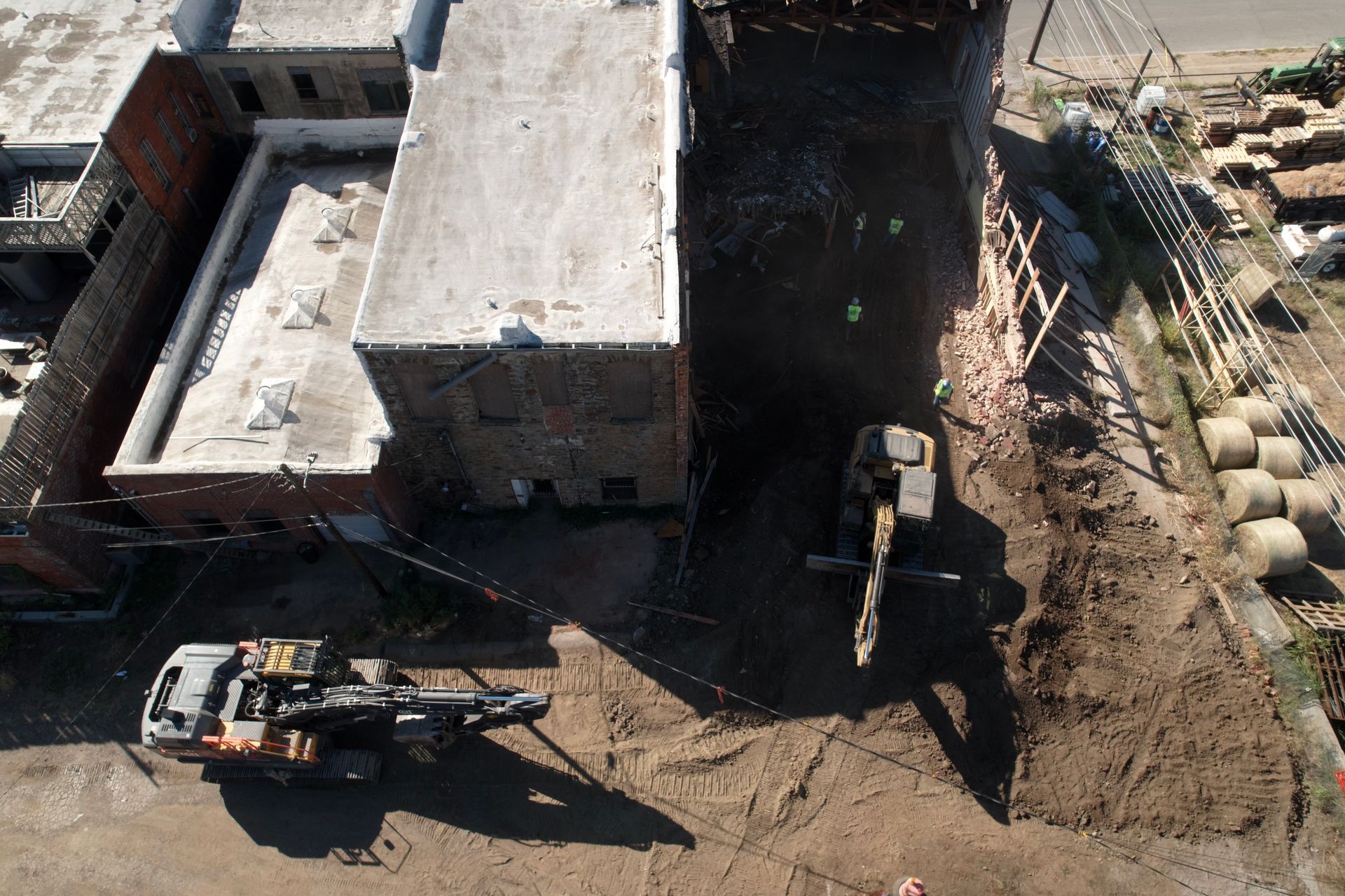 Overhead shot of construction site: Buildings, heavy machinery, dirt, and hay bales.