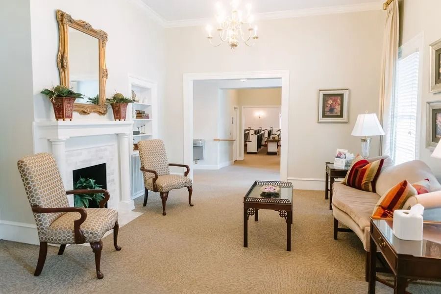 A bright, carpeted seating area with two patterned armchairs, a couch with colorful pillows, a fireplace, and a mirror.