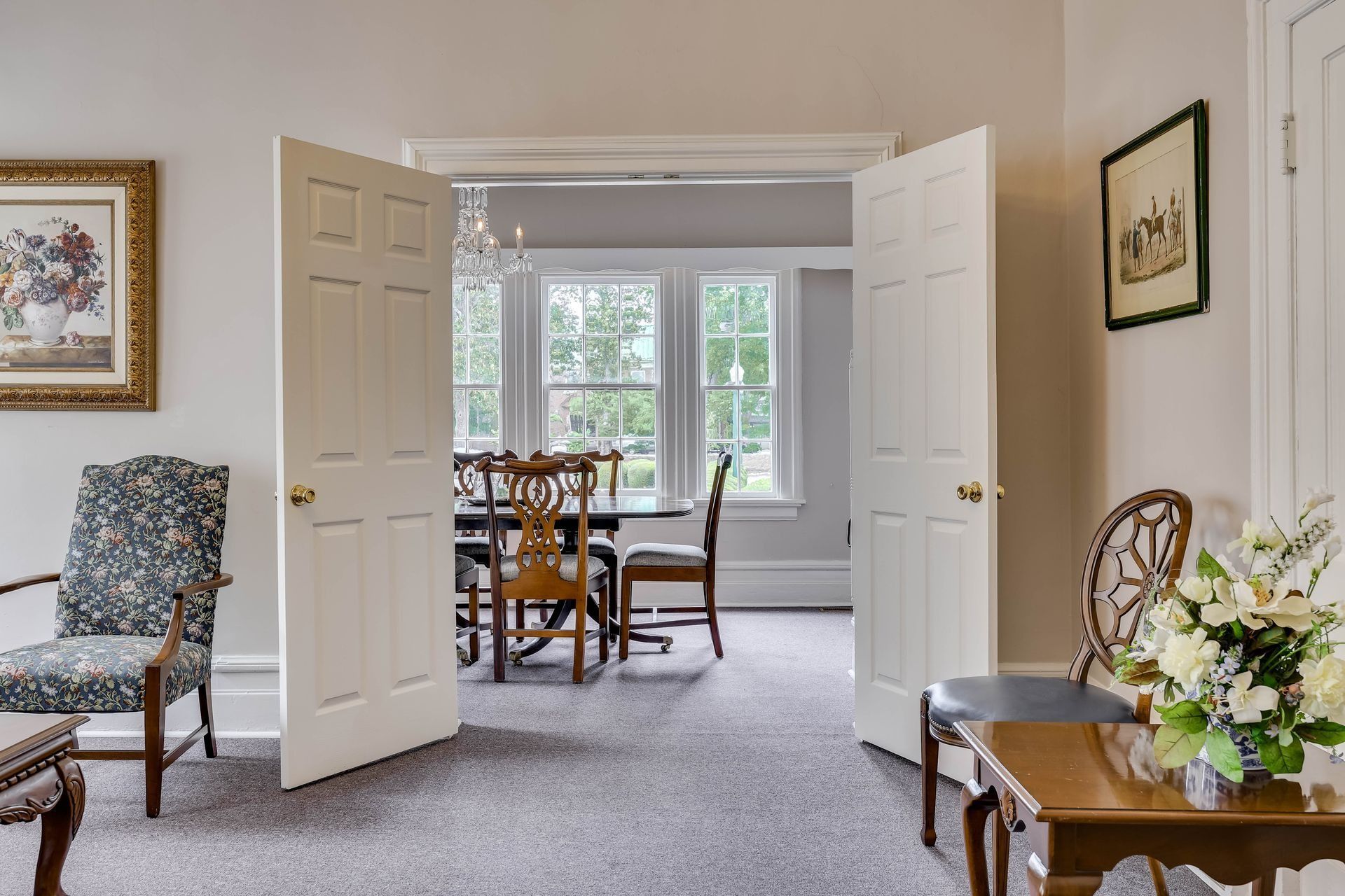 A room view through open white double doors into a dining area with a table and chairs, flanked by two sitting areas.