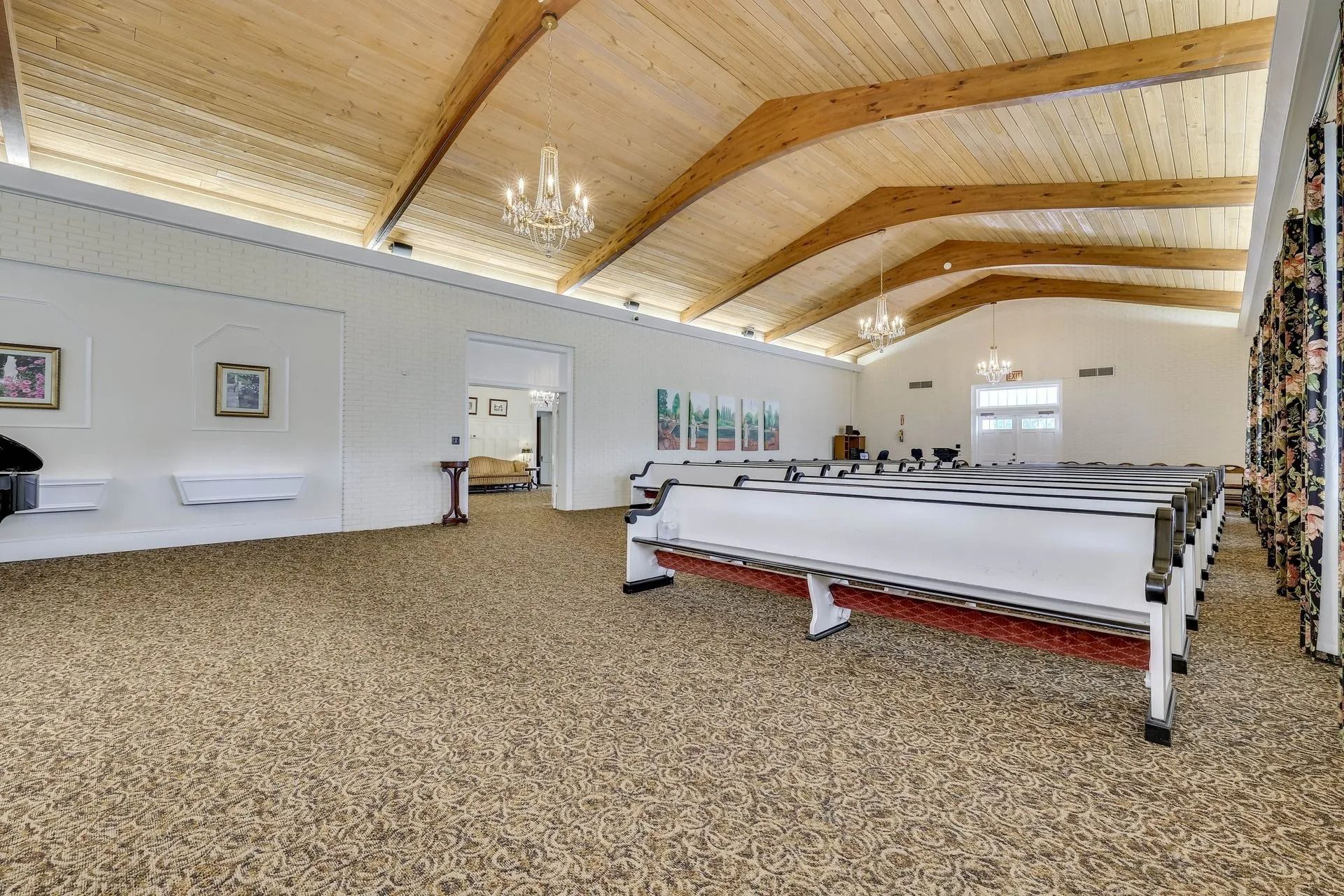 A bright, spacious hall with a vaulted wooden ceiling, speckled flooring, and rows of draped tables arranged for an event.