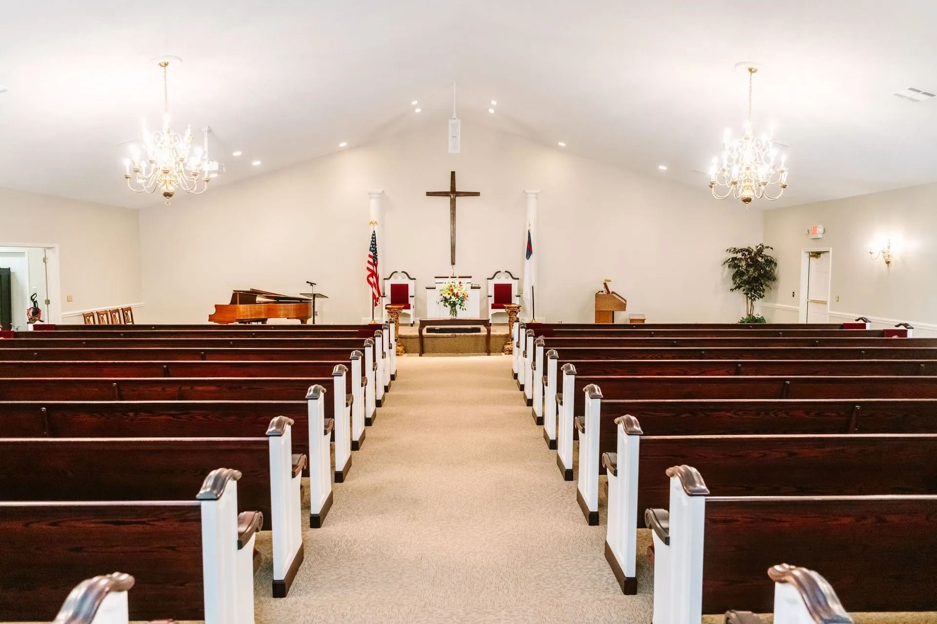 Inside of a church featuring a center aisle with dark wood pews on both sides, leading to a cross on the front wall.