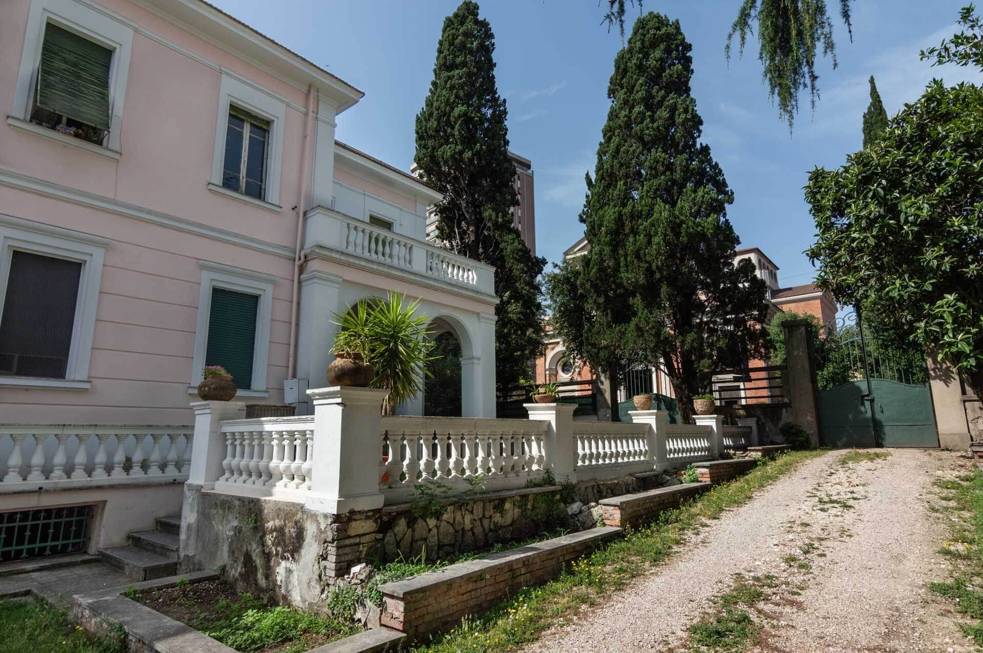 Una casa rosa con una staccionata bianca e alberi davanti