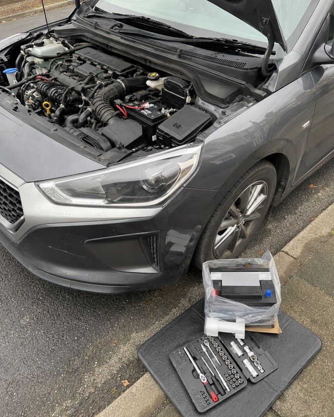 Emergency car battery replacement being carried out by a mobile mechanic on a Coventry residential street