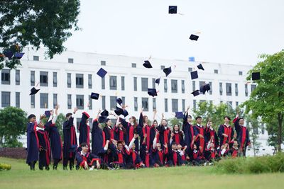Black sedan in a suburban street with a group in graduation caps and gowns gathered behind it