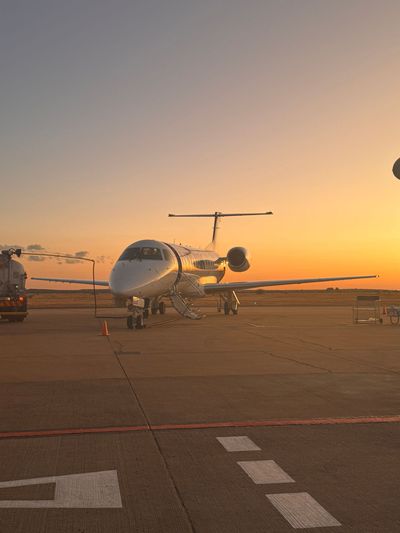Small jet parked on an airport tarmac at sunset under a warm orange sky.