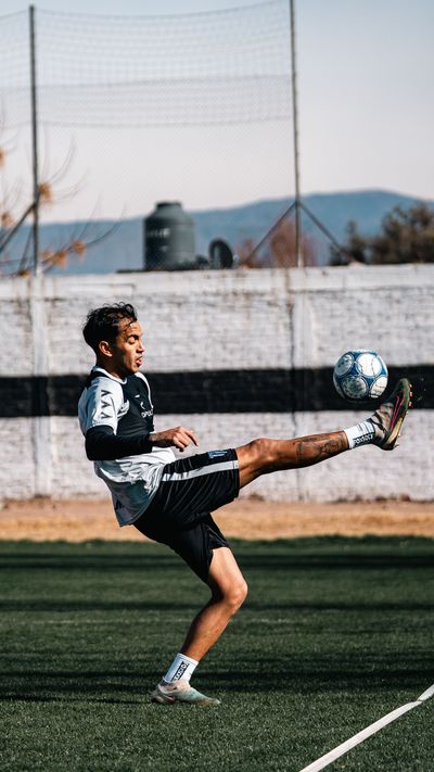 Soccer player in black jersey kicks a ball mid-air on a field