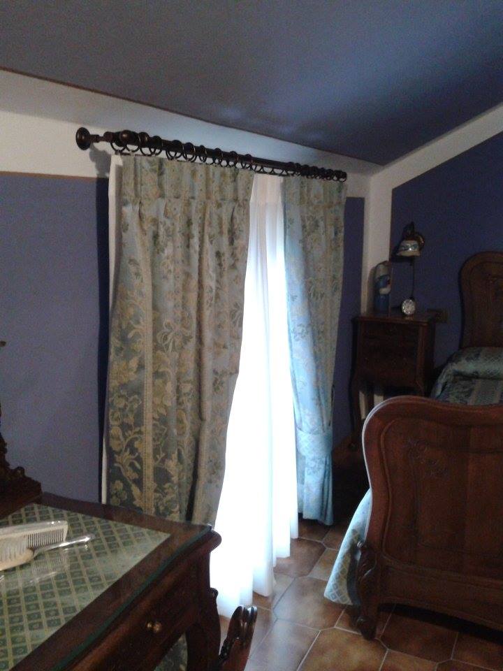 Camera da letto con mobili in legno decorati, tende a fantasia e un comodino con lampada.