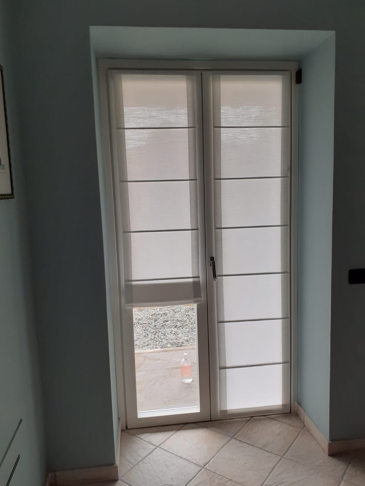 Porta in vetro con cornice bianca, persiane orizzontali e parete azzurra.