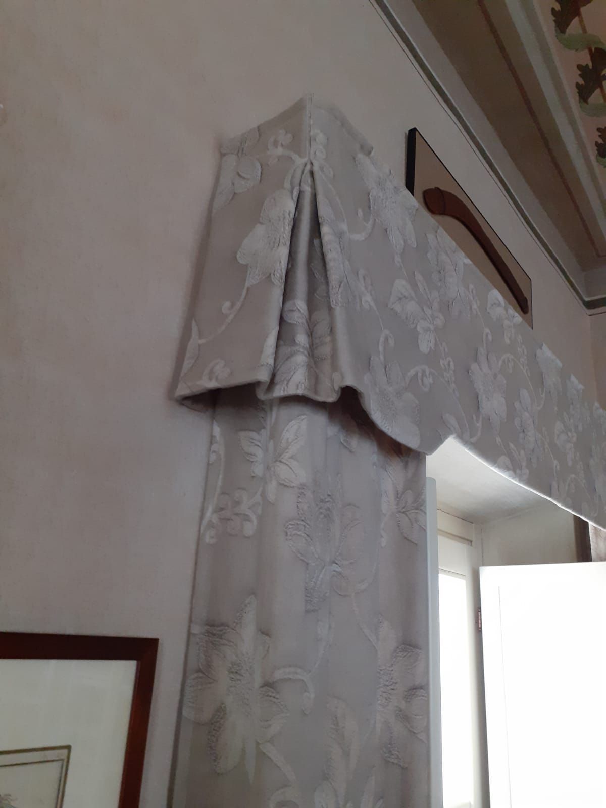 Tenda floreale beige e mantovana sopra una porta, montata su una parete rosa chiaro.