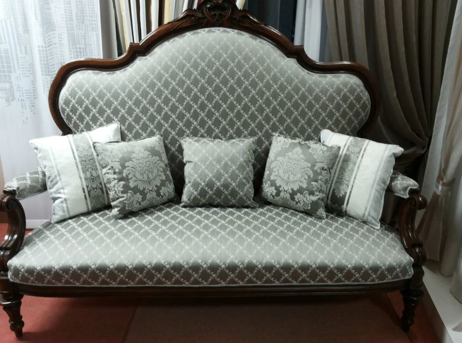 Divano grigio antico con struttura in legno decorato, rivestimento con motivo a rombi e cuscini decorativi.