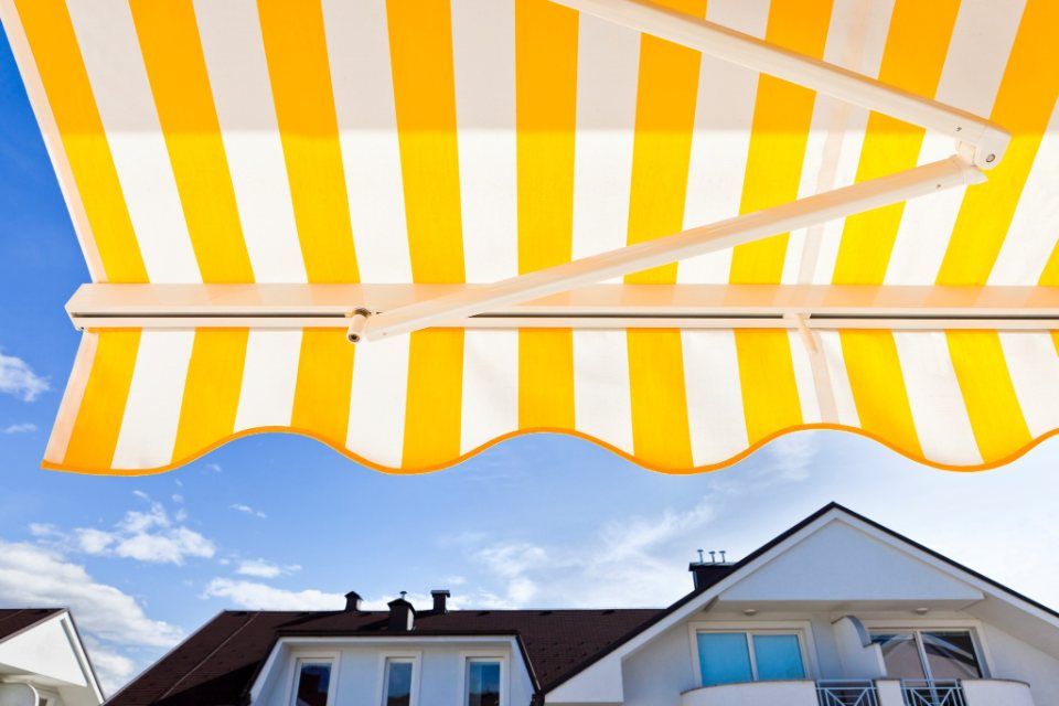 Tenda a strisce gialle e bianche sopra una casa bianca con cielo azzurro sullo sfondo.