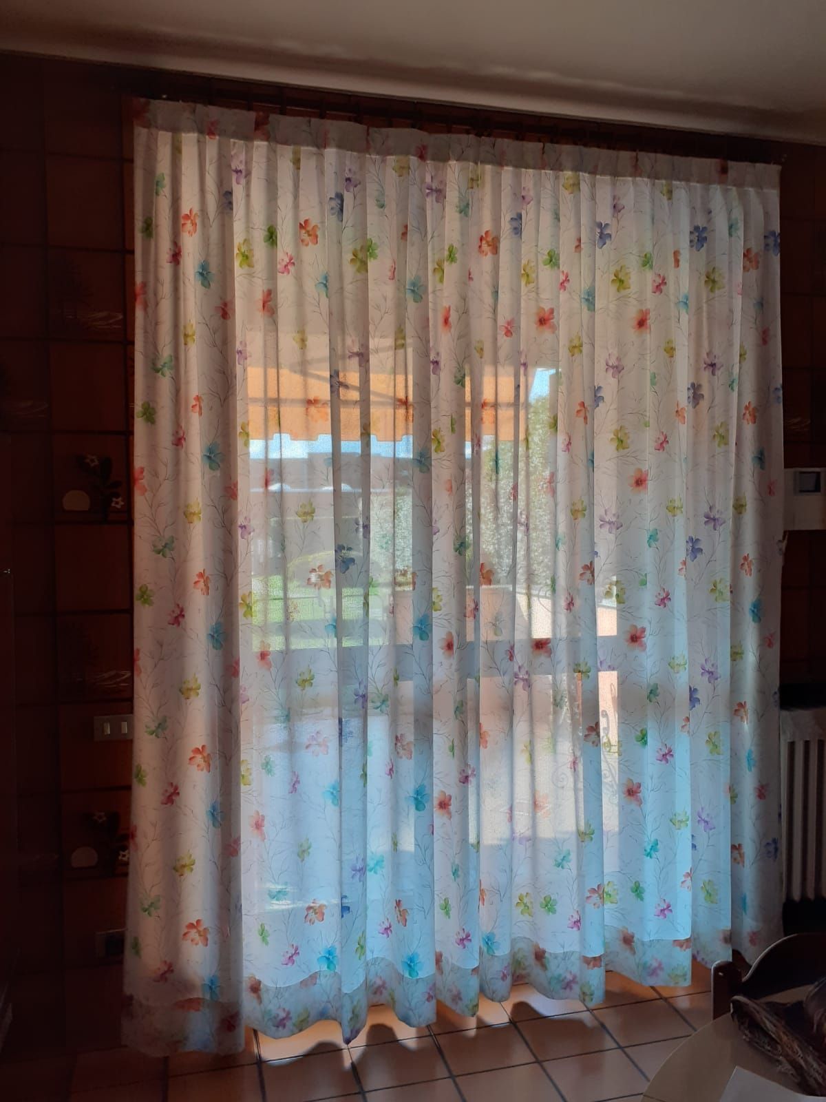 Tenda bianca trasparente con motivo floreale colorato sopra una finestra.