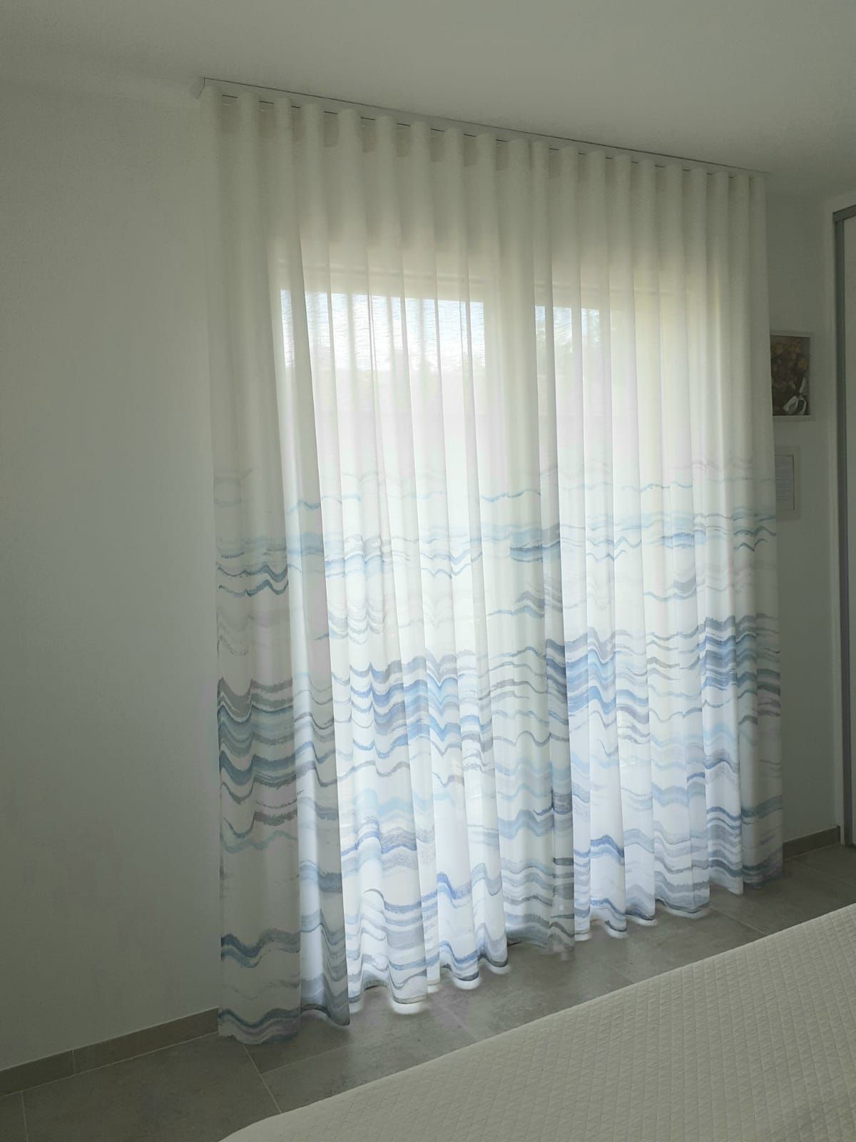 Tende bianche trasparenti con motivo a onde blu, appese davanti a una finestra.