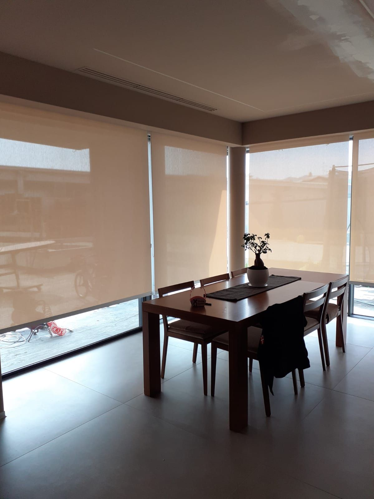 Sala da pranzo con tavolo in legno, sedie e tende alle grandi finestre.