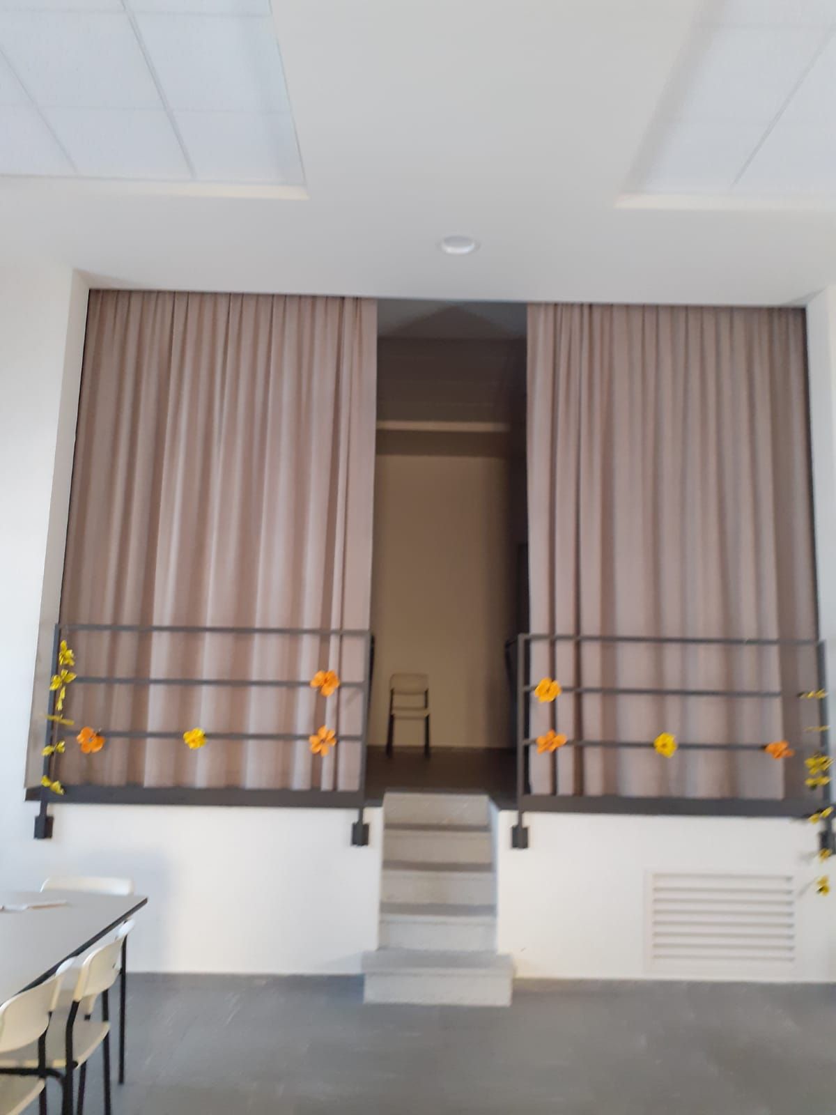 Palco con tende beige chiuse, ringhiera metallica e gradini in cemento. Una sedia è posizionata sul retro.