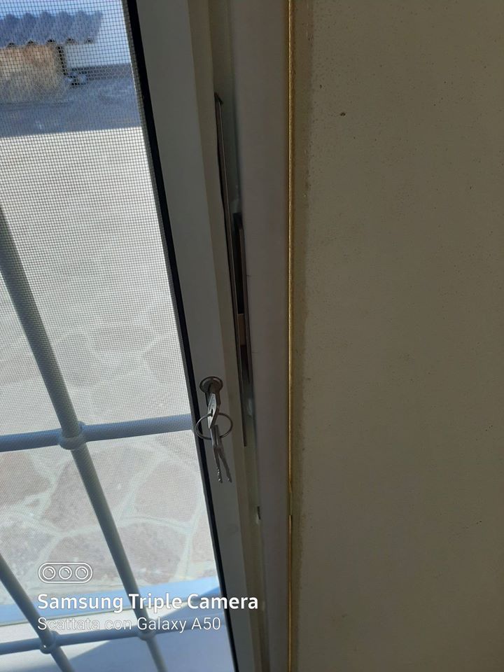 Vista ravvicinata di una porta parzialmente aperta con un chiavistello, che mostra un'area esterna piastrellata sullo sfondo.