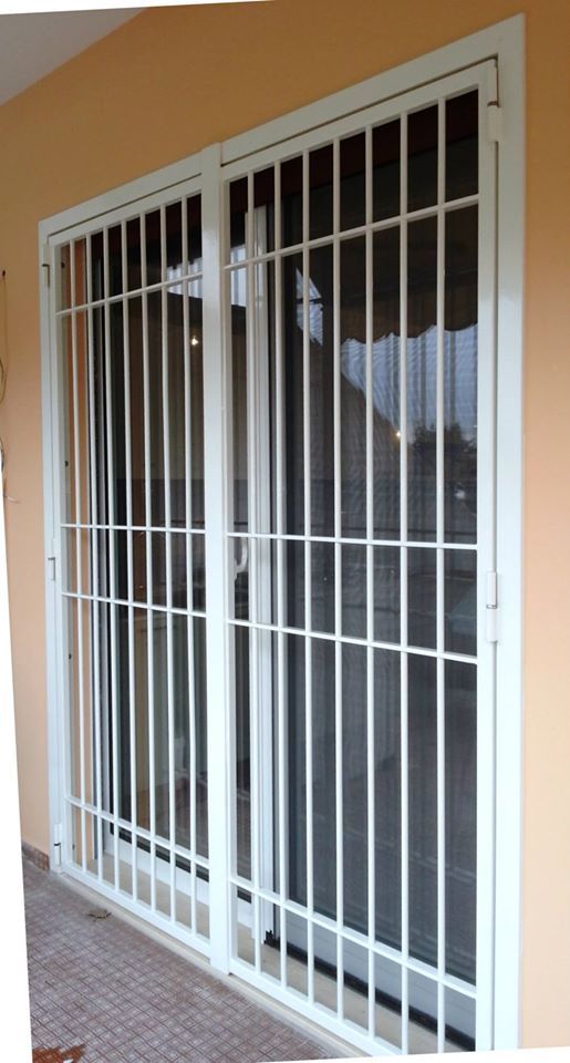 Sbarre di sicurezza bianche sopra una porta scorrevole in vetro scuro su una parete color pesca.