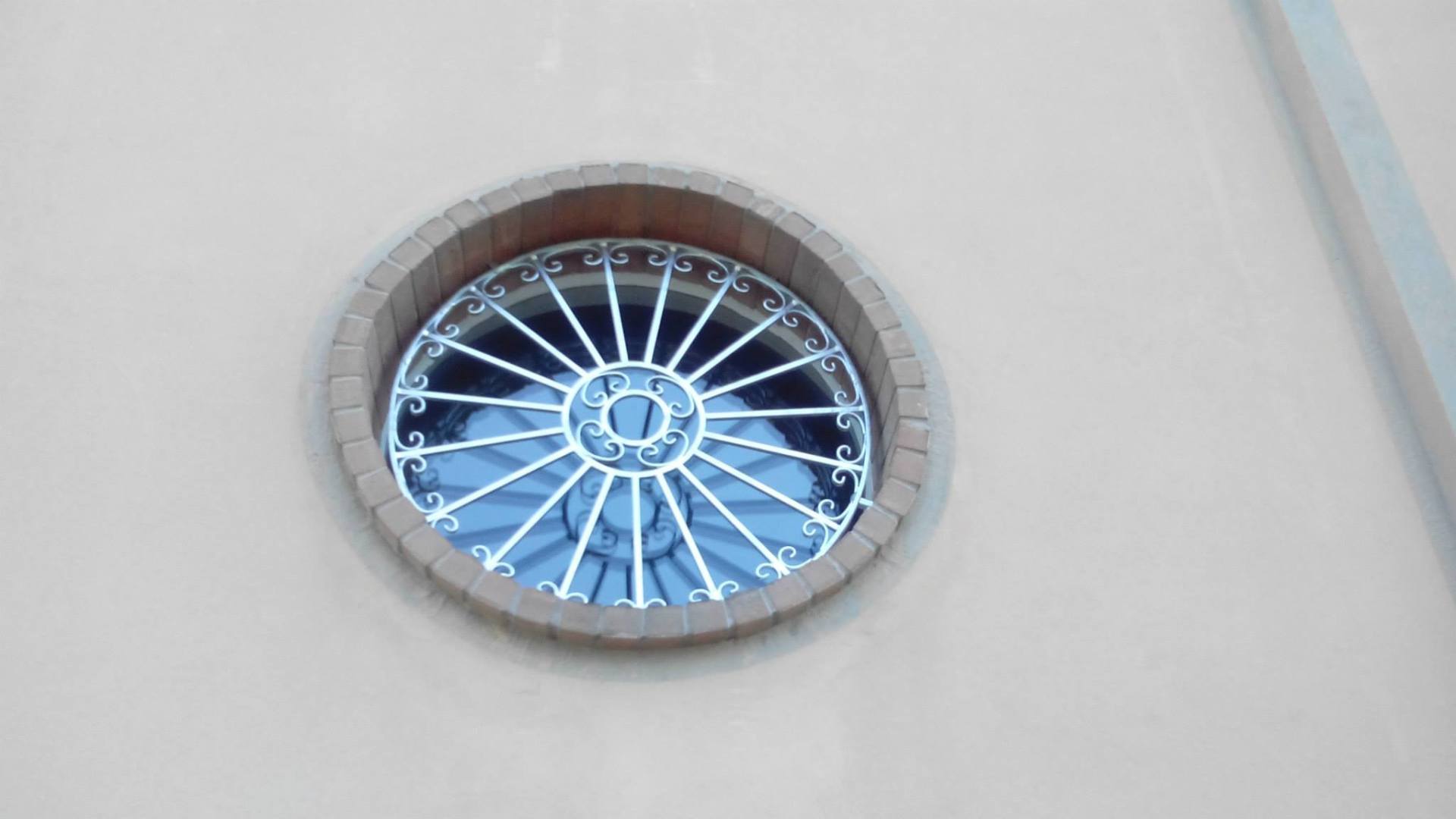Finestra circolare con vetrata blu incastonata in una parete grigio chiaro.