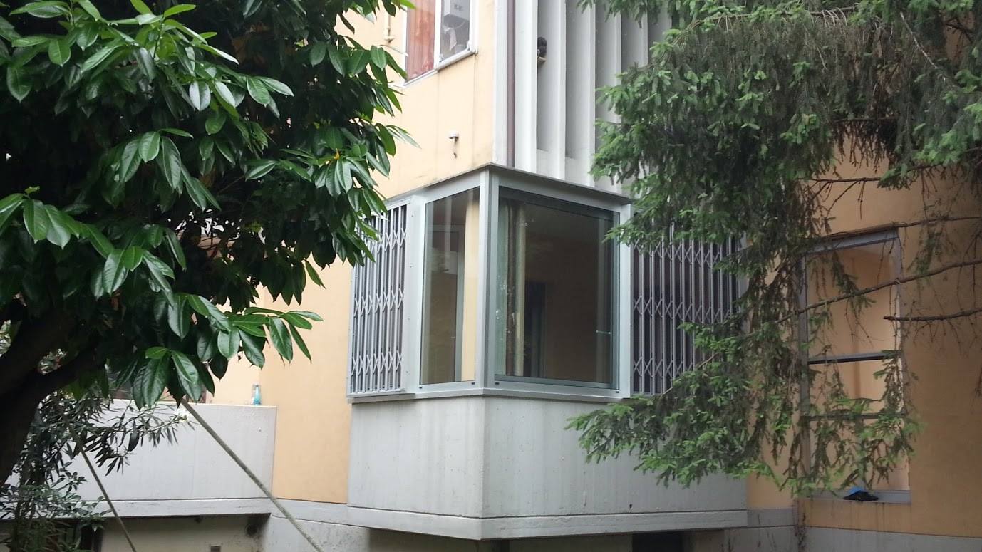 Balcone dell'appartamento racchiuso da una cornice bianca, circondato da alberi e adiacente a un edificio beige.