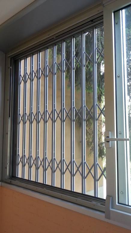 Finestra chiusa con grata di sicurezza in metallo e telaio bianco aperto, vista dall'interno di una stanza.