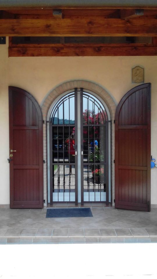 Doppie porte ad arco in legno con cancello in metallo, inserite in un atrio in stucco sotto travi a vista.