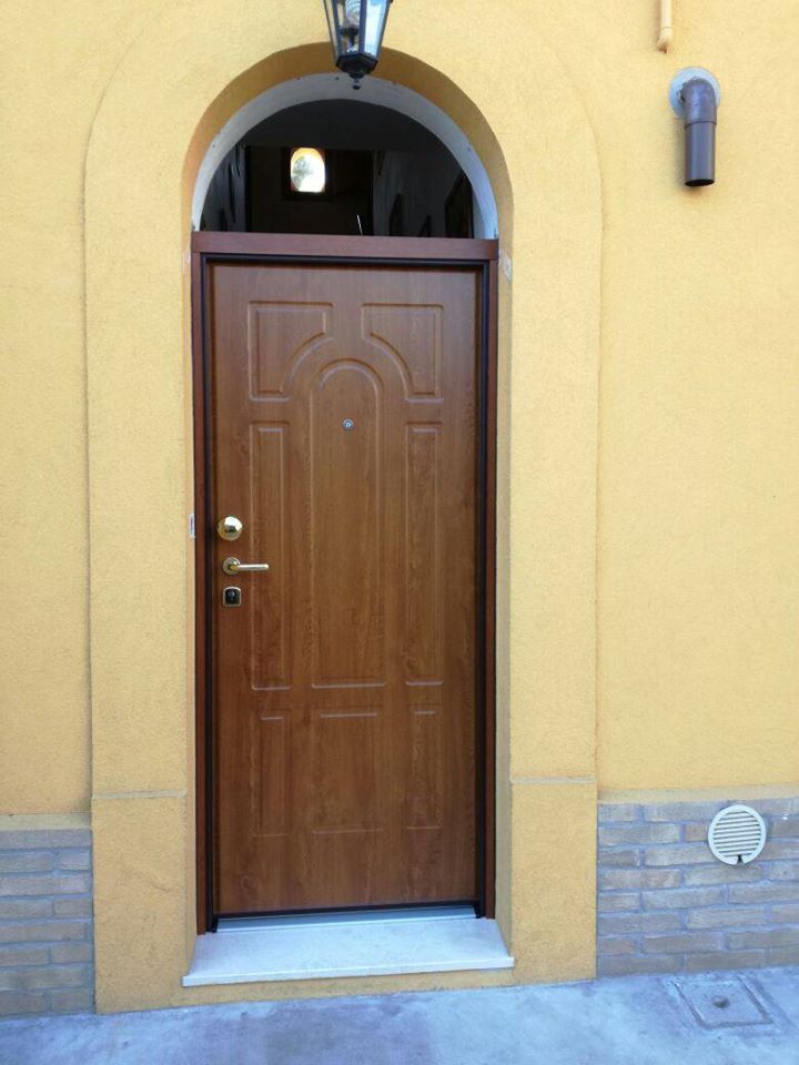 Porta d'ingresso in legno con arco incastonato in una parete di stucco giallo, vista dall'esterno.