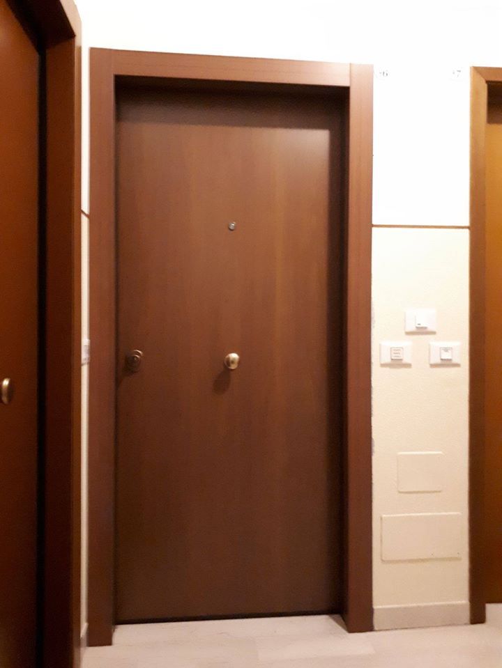 Porta d'ingresso marrone dell'appartamento in un corridoio con pareti beige e interruttori della luce