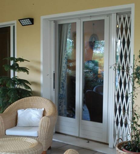 Porta scorrevole in vetro con cancello di sicurezza a soffietto bianco accanto a una sedia in vimini in una veranda.