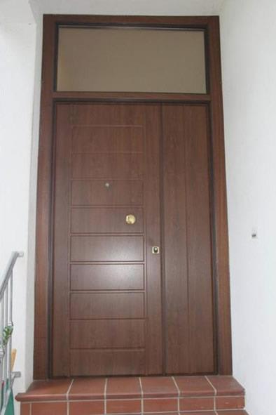 Porta d'ingresso in legno marrone con sopraluce, incastonata in un muro bianco sopra una scalinata in mattoni.