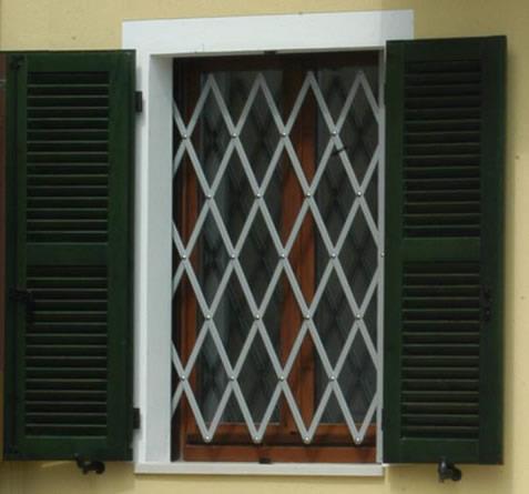 Finestra chiusa con persiane verdi e grata di sicurezza in metallo bianco su un muro giallo.