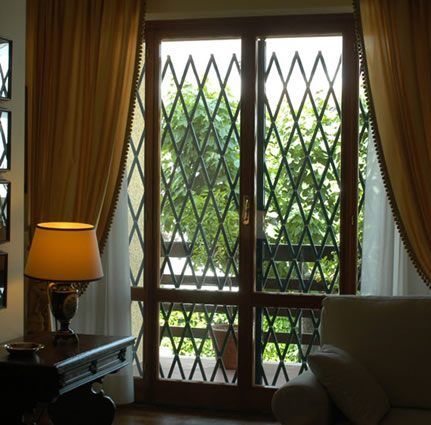 Soggiorno con grate di sicurezza alle finestre, tende, lampada da comodino e vista sul giardino.