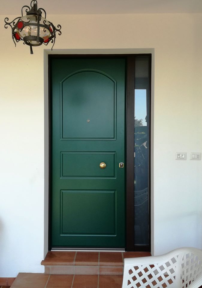 Porta d'ingresso verde con pomello in ottone e pannelli laterali in un ingresso piastrellato.