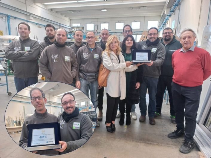 Gruppo in posa durante un workshop, due persone che reggono premi incorniciati, con un primo piano del certificato in riquadro.
