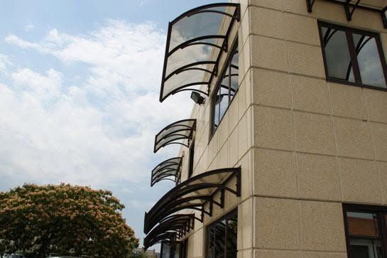 Esterno di un edificio moderno con tettoie metalliche curve contro un cielo nuvoloso.