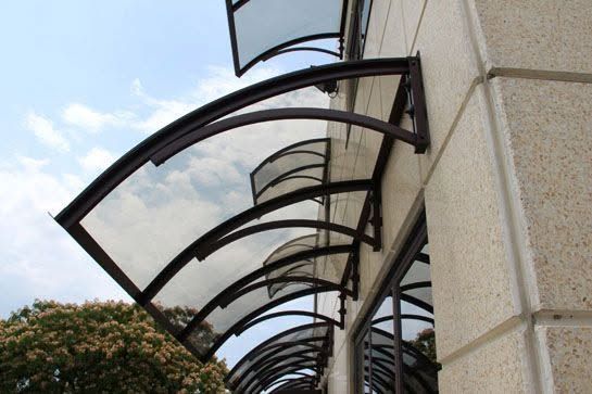 Tende da sole nere e curve lungo un edificio beige sotto un cielo parzialmente nuvoloso