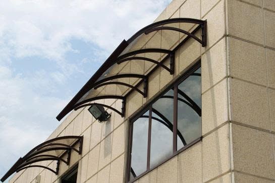 Tende da sole nere e curve sopra le finestre di una facciata di un edificio beige, sullo sfondo di un cielo nuvoloso.
