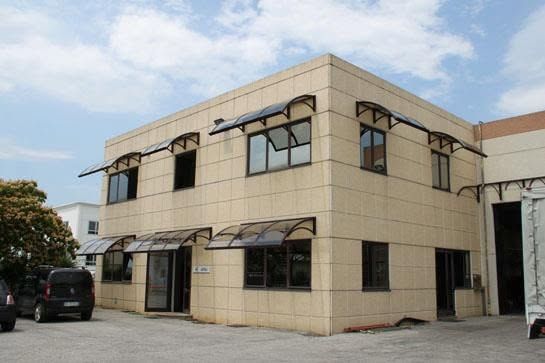 Edificio per uffici beige a due piani con tende da sole nere e auto parcheggiate davanti.