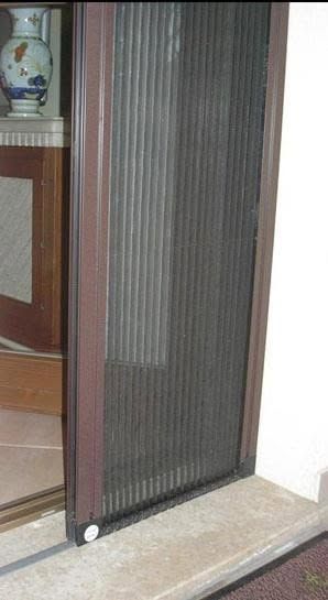 Zanzariera a rete nera in una porta accanto a un mobile in legno e una parete bianca.