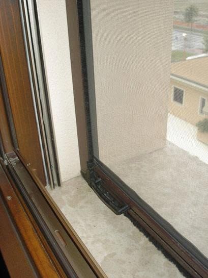 Finestra aperta con zanzariera e binario accanto alla facciata di un edificio beige.