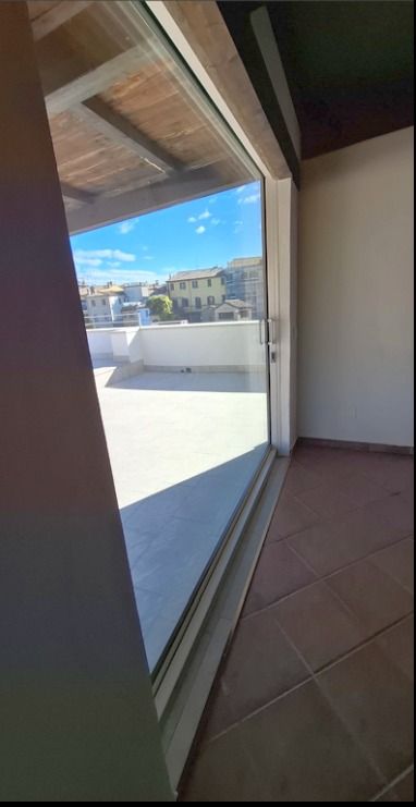 Porta scorrevole in vetro che dà su una terrazza panoramica soleggiata, con pavimento piastrellato, pareti bianche e cielo azzurro all'esterno.