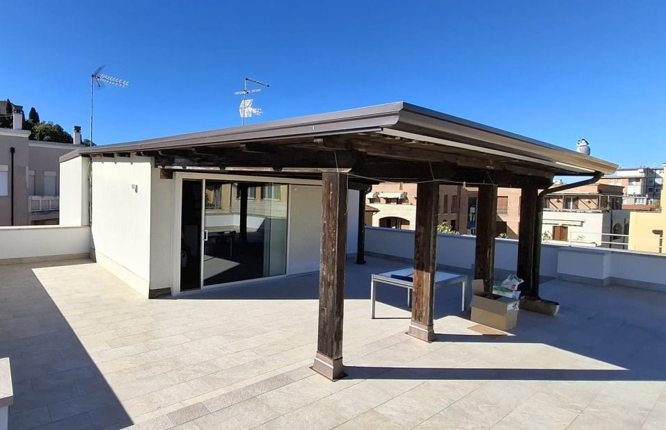 Moderna terrazza sul tetto con pergolato in legno, porte a vetri e pareti bianche sotto un cielo azzurro limpido.
