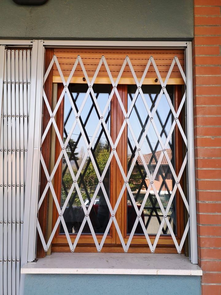 Cancello di sicurezza in metallo bianco sopra una finestra con persiane arancioni su un muro di mattoni