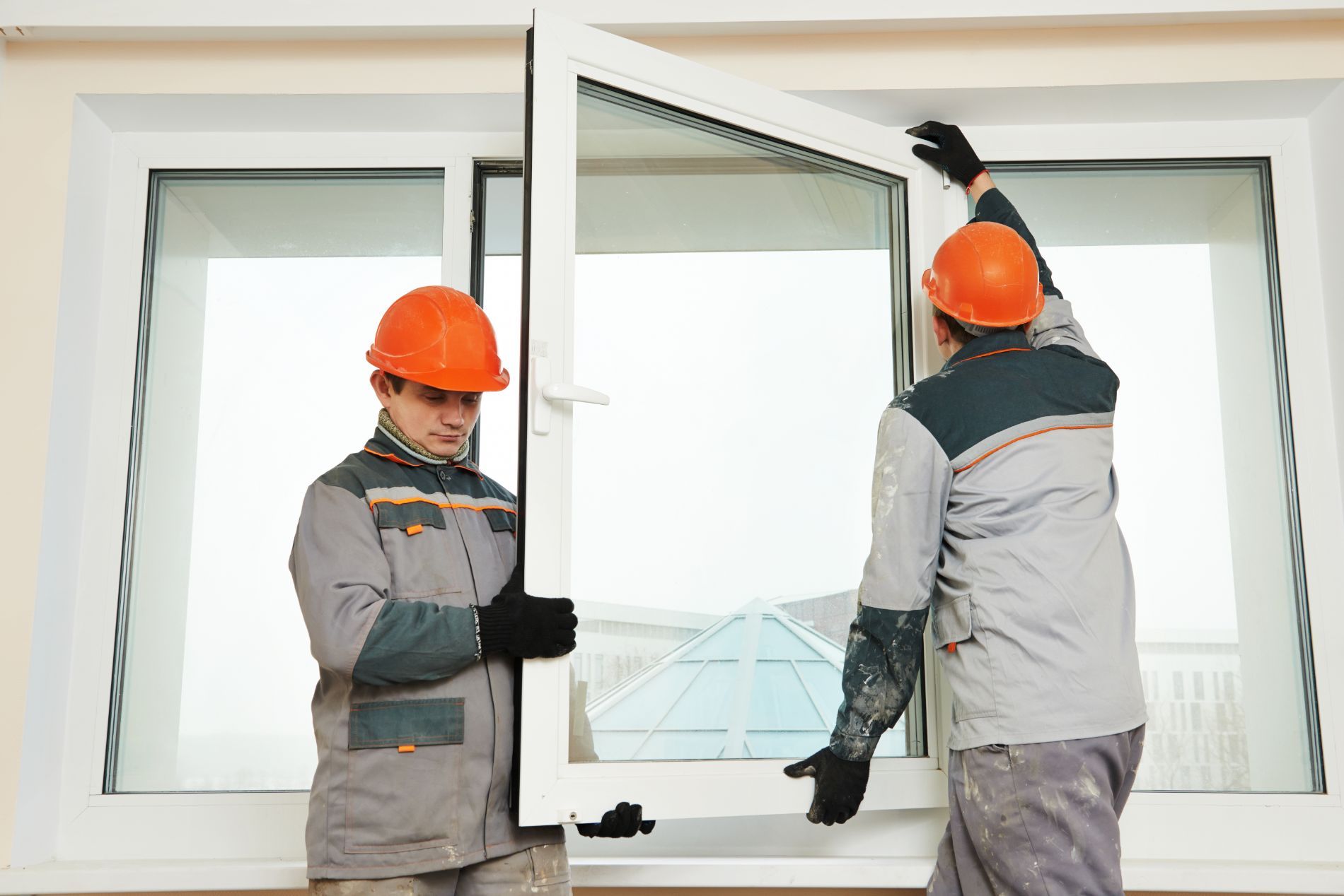 Due operai con elmetti di sicurezza installano un telaio di finestra all'interno.