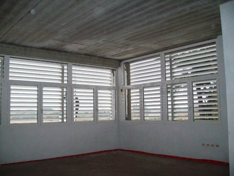 Stanza bianca vuota con finestre a persiana e pavimento grigio sotto un soffitto rivestito in legno.